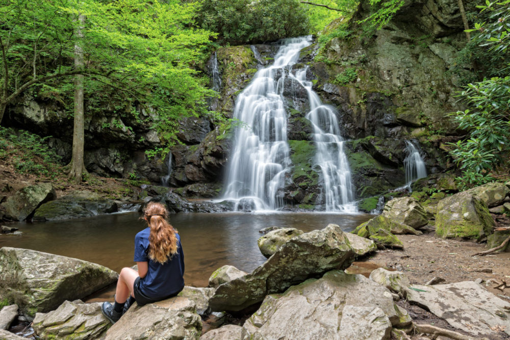 Young woman sitting on a rock viewing Spruce Flat Falls, a beautiful cascading waterfall, in Tennessee