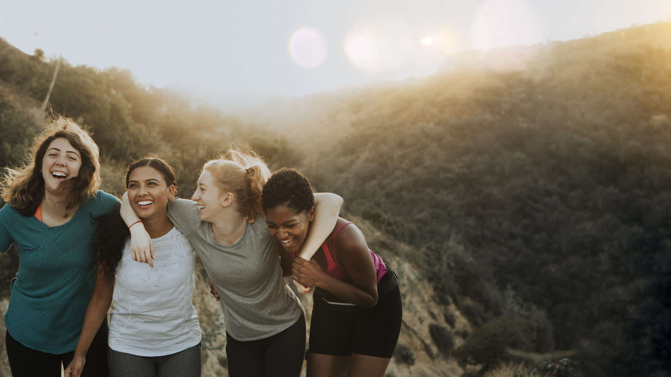 Four friends hiking through rolling hills and laughing and smiling