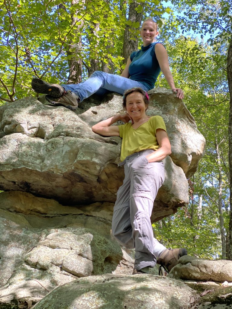 Two women posing on top of a natural rock feature in the forest