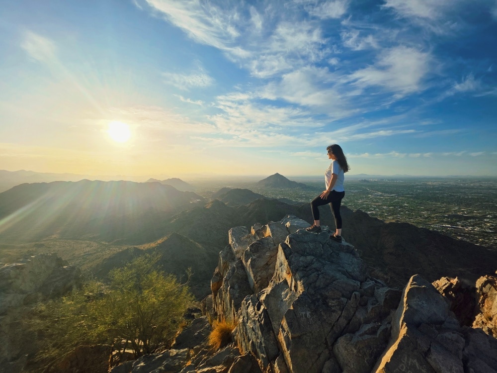 A woman standing at the summit of Piestewa Peak during sunrise
